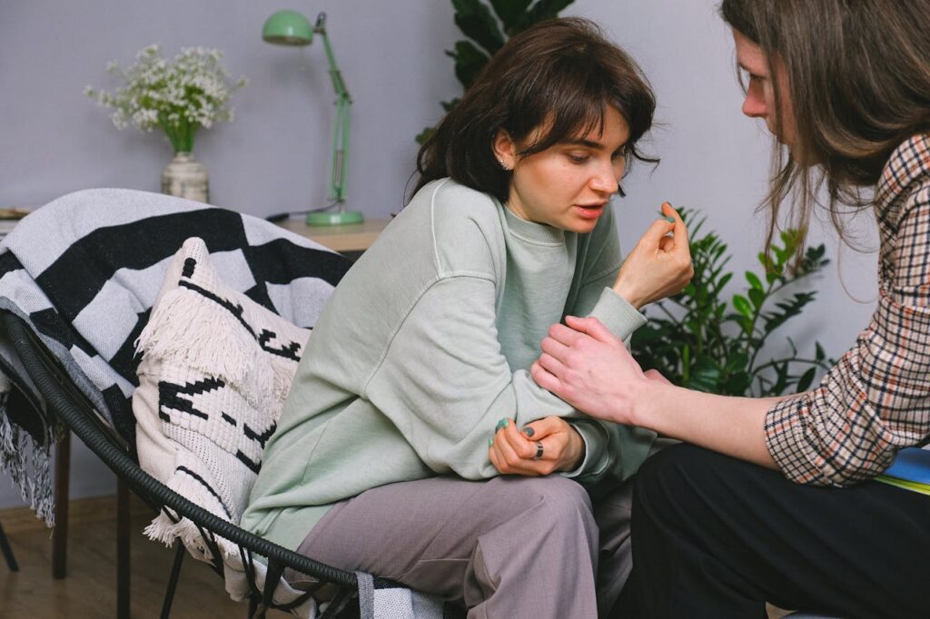 Crop psychotherapist holding adult woman by arm while talking during psychological session in light house